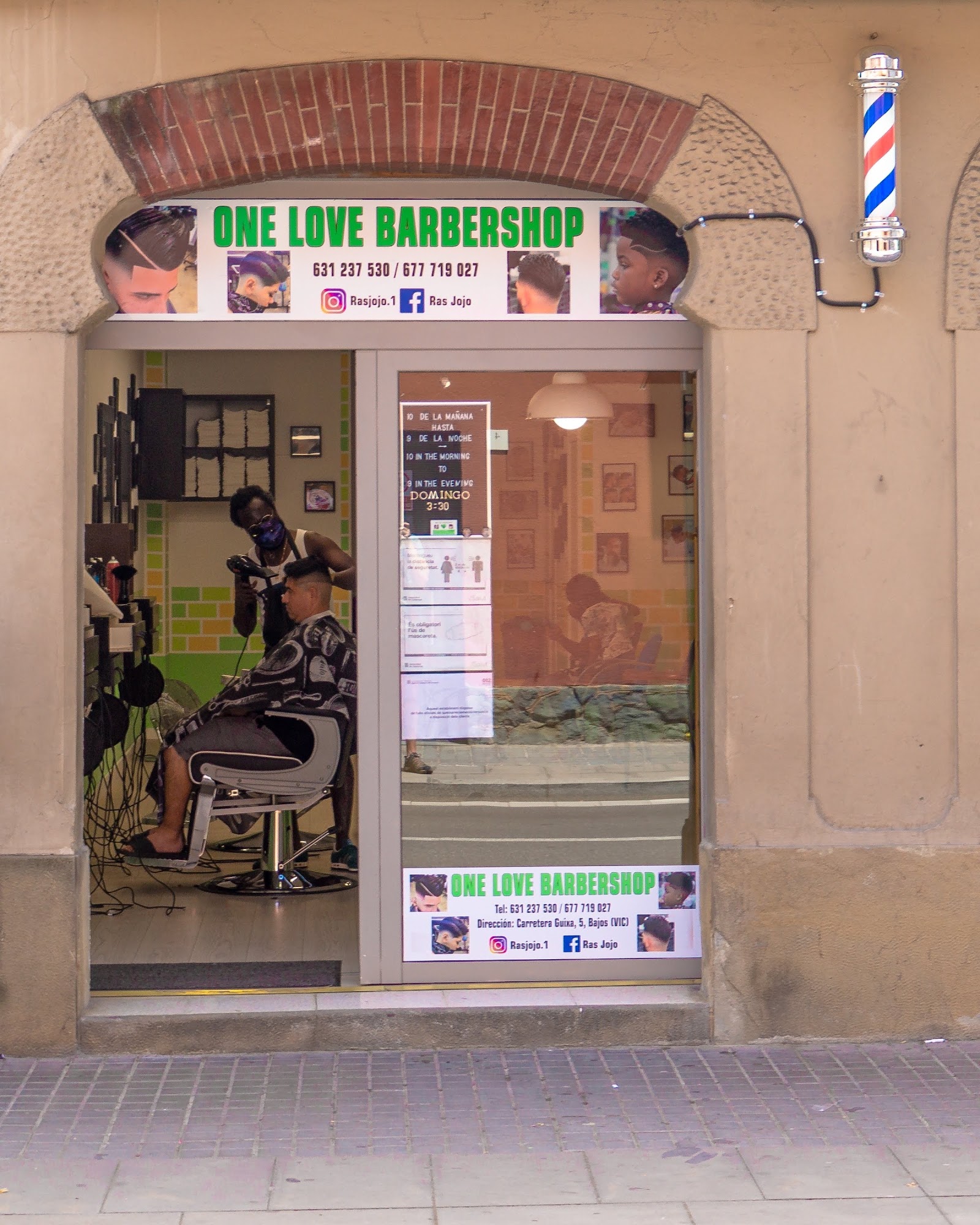 The entrance to Perruqueria One Love Barbershop, with a barber at work inside